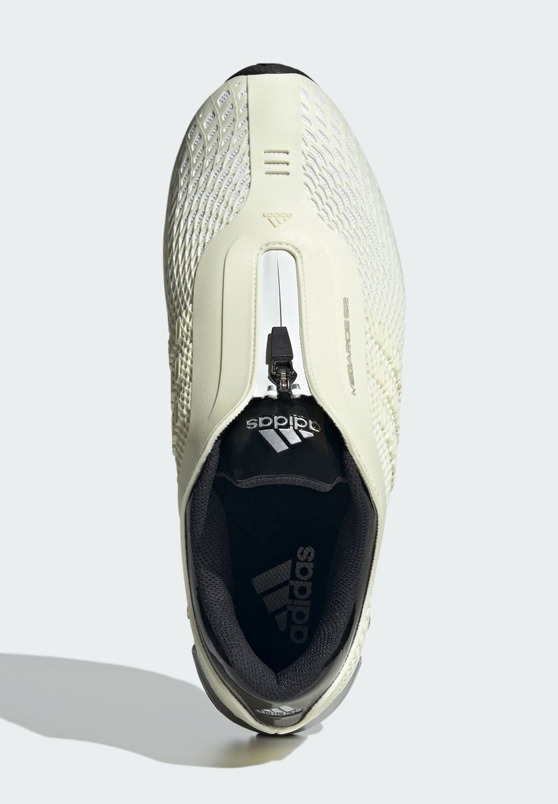 Cremefarvet sportsko med en struktureret mesh-overdel, lynlåsclosure, sort indvendig, og sølvlogo detaljer. Rundt tå og polstret krave.