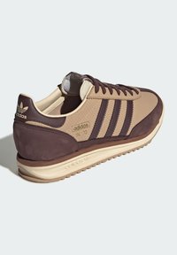 Baskets Adidas marron et beige en matériaux daim et cuir, présentant trois rayures sombres, une tige texturée et une semelle en caoutchouc.