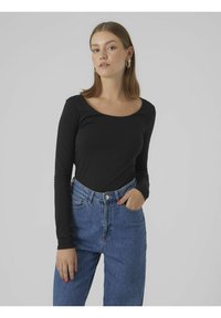 Schwarzes langärmliges Oberteil mit Rundhalsausschnitt, kombiniert mit hochgeschnittenen blauen Jeans aus Denim mit heller Waschung und dezenten Nähdetails.