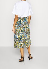 Falda midi con estampado floral en tonos azules, amarillos y morados, confeccionada en una tela ligera con un dobladillo acampanado, complementada con una blusa blanca lisa.