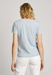 Gaiši zils kokvilnas T-krekls ar īsām piedurknēm un apaļu izgriezumu, redzams no aizmugures, salikts kopā ar baltām biksēm. Gluda tekstūra.