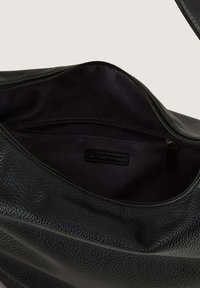Interno di una borsa a tracolla nera in pelle con una finitura texturizzata, dotato di una tasca con cerniera e un'etichetta del marchio. Rivestimento liscio e scuro.