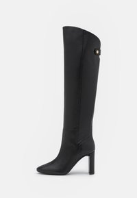 Botte noire en simili cuir montante avec bout pointu,Talons aiguilles et un détail de bouton sur le côté ; texture lisse et design épuré.