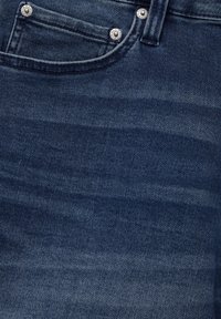 Jean en denim bleu foncé avec une poche avant dotée de quincaillerie argentée et de légères variations de texture sur le tissu.