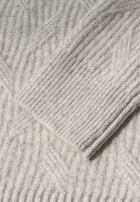 Lichtgrijze gebreide trui met een textuur, voorzien van een zigzagpatroon en geribde mouwmanchetten. Gemaakt van zachte, warme stof met een merkbare diepte.