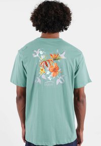 T-shirt manches courtes vert menthe avec des motifs floraux au dos, coupe décontractée et texture douce. Marque "Oxbow" incluse.