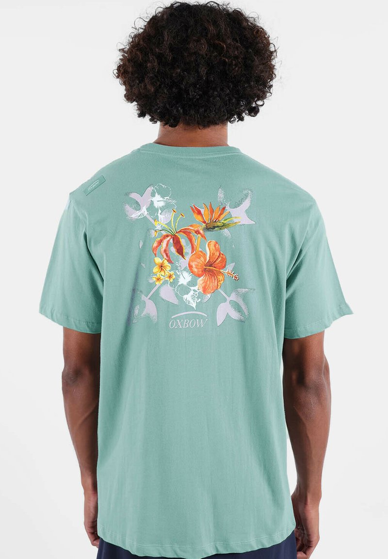 T-shirt manches courtes vert menthe avec des motifs floraux au dos, coupe décontractée et texture douce. Marque "Oxbow" incluse.