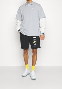 Gray short-sleeve polo with white Nike logo, paired with black shorts featuring colorful Nike branding, white sneakers, and yellow socks.