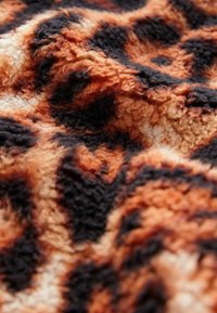 Tissu à motif léopard avec une texture fuzzy. Les couleurs incluent l'orange, le noir et la crème dans un motif abstrait avec des fibres douces et en relief.