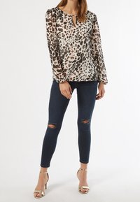 Blusa in stampa leopardata con maniche lunghe e a palloncino e scollatura a oblò. Indossata con jeans skinny scuri con strappi sulle ginocchia e tacchi a rocchetto dorati.