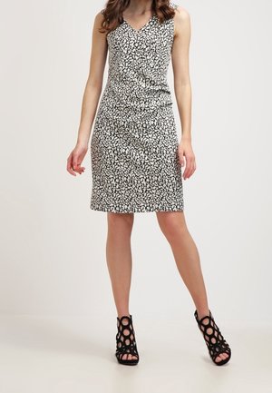 Donna che indossa un vestito senza maniche a motivo bianco e nero, lungo fino al ginocchio, con scollo a V e scarpe nere con tacco alto e punta aperta.