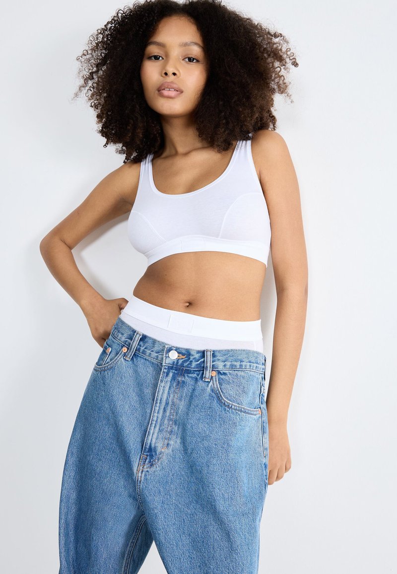Witte katoenen bralette met een dunne band, gecombineerd met lichtblauwe, high-waisted spijkerbroek met een relaxte pasvorm en zichtbare stikseldetails.