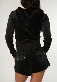 Svart velour hoodie med mjuk textur, med en huva och ribbad midja. Parat med matchande shorts som har fickor med klaff och tryckknappar.