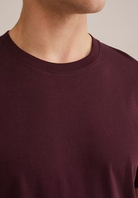 Burgundska majica s kratkim rukavima i okruglim izrezom, izrađena od glatkog pamučnog materijala. Ima kratke rukave i bezšavne izreze, prikazujući solidnu boju bez uzoraka.