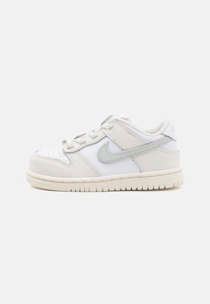 Weißes Leder-Sneaker mit hellgrauen Akzenten, runder Zehenpartie, Schnürdesign und einer strukturierten Gummisohle. Nike-Logo an der Seite.