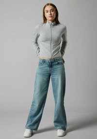 Haut à manches longues zippé gris associé à un jean large bleu clair. La tenue présente un motif décontracté, une texture lisse et des baskets blanches.