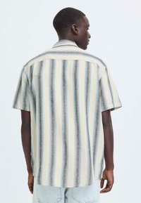 Overhemd met korte mouwen van lichtgewicht stof met verticale strepen in beige, blauw en bruine tinten; klassieke kraag en losse pasvorm.