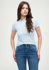 Lichtblauw t-shirt met korte mouwen gecombineerd met blauwe jeans. Het t-shirt heeft een ronde halslijn en een nauwsluitend ontwerp, met een gladde textuur.