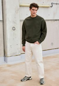 Olivgrüner Fleece-Pullover, weiße Jeanshose und graue Turnschuhe. Das Outfit hat eine lockere Passform und gerippte Akzente an den Bündchen und am Saum.