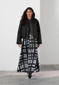 Giubbotto bomber imbottito nero, top grigio e gonna maxi con un audace motivo a quadri bianchi e navy. Presenta maniche lunghe ed elastici ai polsi.