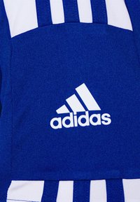 Blå sportstopp med vita accenter, tre ränder design och en framträdande vit Adidas-logotyp på bröstet. Tillverkad av strukturerad tyg.