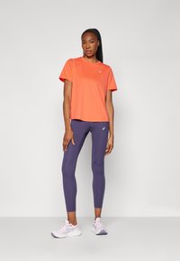 Orange short-sleeve athletic top paired with form-fitting purple leggings. Features a logo on the top and light purple running shoes.