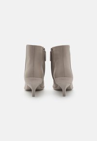 Botines de cuero taupe claro con un tacón delgado y curvado, y cremallera lateral, con un logotipo grabado en la parte posterior.
