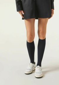 Marineblå knæhøje sokker lavet af et glat, strækbart stof, parret med hvide sneakers. Simpelt design, ingen synlige mønstre eller udsmykninger.
