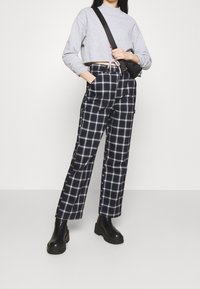 Felpa grigia corta con orlo regolabile, abbinata a pantaloni a quadri bianchi e neri. I pantaloni presentano tasche laterali e un design a gamba larga. Scarpe con tacco nero.