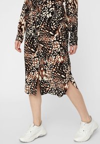 Abito lungo a fantasia nei toni del nero, marrone e crema, con maniche lunghe, vita con laccio e aperture laterali, abbinato a sneakers bianche.