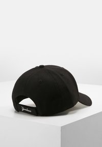 Casquette de baseball noire avec une visière courbée, fabriquée en tissu texturé. Équipée d'une sangle ajustable et d'une étiquette "Yankees" à l'arrière.