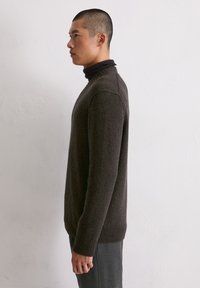 Dunkelbrauner Strickpullover mit gerippten Bündchen und Saum, ausgestattet mit einem Rundhalsausschnitt und einer lässigen Passform, getragen über einem schwarzen Rollkragenpullover.