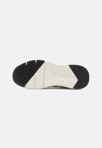 Semelle de sneakers noire et blanche avec un fond en caoutchouc texturé présentant un motif en vagues et un logo en relief sur le côté pour une traction et une durabilité accrues.