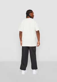 Lichtgrijze oversize t-shirt met korte mouwen, gecombineerd met zwarte cargobroek met zijzakken en witte sneakers.