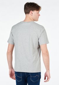 T-shirt grigio a maniche corte in un tessuto morbido, con colletto tondo e taglio dritto, indossato con jeans blu. Nessun motivo o logo visibile.