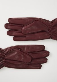Guantes de cuero burdeos con muñecas fruncidas, que cuentan con cuatro espacios para los dedos y un espacio para el pulgar, realzados por costuras en contraste.