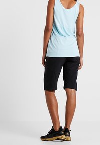 Světle modrý sportovní top s volnějším střihem, kombinovaný s černými kraťasy po kolena a černými teniskami se zlatými detaily.