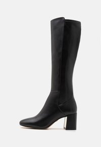 Botte en cuir noir montée jusqu'au genou, à bout pointu, avec un talon carré et une silhouette épurée. Présente des coutures minimales et une texture lisse.