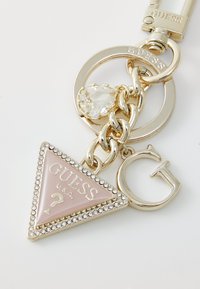 Keychain featuring a pink triangular charm with "GUESS U.S.A." text, surrounded by rhinestones, attached to a gold-toned chain and metal rings.