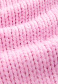 Puha rózsaszín kötött anyag, feltűnő, vastag öltésekkel és bolyhos textúrával, amely szőtt mintákat és enyhe fényes csillogást mutat természetes fényben.