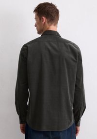 Chemise boutonnée vert foncé avec de longues manches, un col classique et un tissu doux et texturé. Présente des poignets à boutons et un ourlet arrondi.