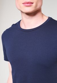 Námořnická modrá bavlněná trička s kulatým výstřihem, krátkými rukávy a hladkým povrchem; přiléhavý styl zdůrazňuje trup.