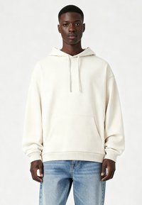 Kremo spalvos bliuzonas su priekinėmis kišenėmis, reguliuojamomis raištelėmis ir gumuotais rankogaliais. Pora su šviesiai mėlynomis džinsinėmis kelnių. Kasdienis dizainas.