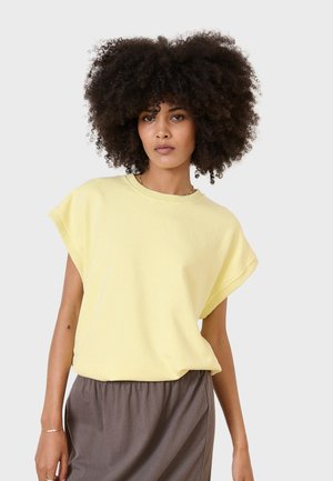 Yellow cotton short-sleeve t-shirt with raw edges. Loose fit with a crew neckline. Paired with a gray elastic-waist skirt.
