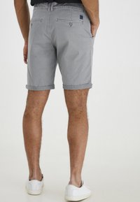 Shorts en coton gris avec un tissu légèrement texturé, des poignets retroussés et des poches arrière. Associés à des baskets blanches.