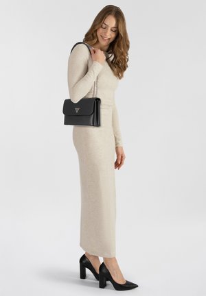 Abito lungo a maniche lunghe beige, realizzato in morbido tessuto knit, abbinato a una borsa in pelle nera con dettagli in catena argento e un logo triangolare.