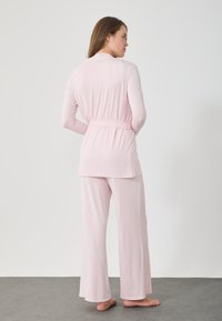 Ροζ πιτζάμα με μακριά μανίκια, συνοδευόμενη από κορδόνι στη μέση και ταιριαστά παντελόνια με φαρδιά πόδια, κατασκευασμένη από μαλακό, λείο ύφασμα.