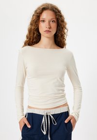 Haut créme à manches longues avec un décolleté bateau, en tissu doux, au design ajusté, porté avec un pantalon bleu marine doté d'une taille rayée et d'un cordon de serrage.