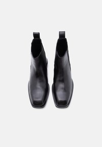 Ζευγάρι μαύρες δερμάτινες μπότες Chelsea με τετράγωνες μύτες και θηλιές για τράβηγμα, εμφανιζόμενες από πάνω σε λευκό απλό φόντο.