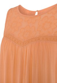Pfirsichfarbene Bluse mit einem floralen Spitzeneinsatz im oberen Teil, strukturiertem Oberteil und zarter Raffung am Saum. Schlüsselloch-Verschluss mit Knopfdetails hinten.